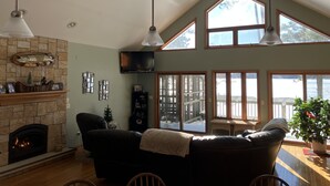 Ein geräumiges Wohnzimmer mit Kamin, einem großen Fernseher und Seeblick durch große Fenster.