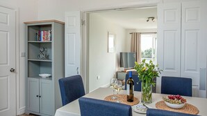 Un coin repas avec une table dressée pour deux personnes, une bibliothèque et une vue sur une autre pièce.