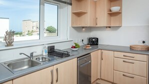 Une cuisine moderne dotée d’un évier en acier inoxydable, d’un lave-vaisselle, de meubles en bois et d’une fenêtre avec des stores.