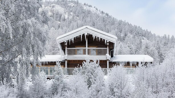 Eine Blockhütte mit Balkon, umgeben von schneebedeckten Bäumen und einem Berg im Hintergrund.