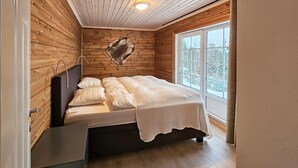 Ein Zimmer einer Holzhütte mit einem Bett, einem Fenster und einer Deckenleuchte.