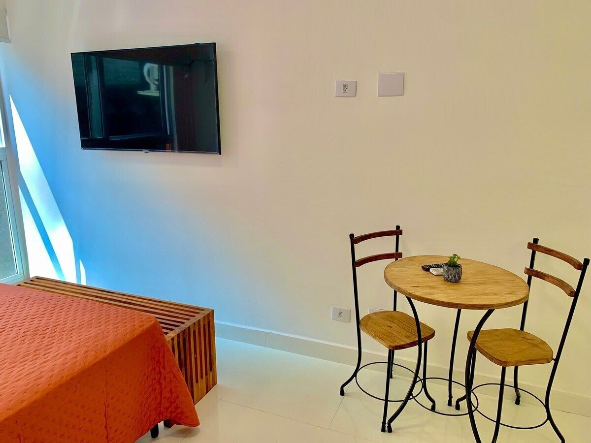 Una habitación con una cama, un televisor montado en la pared, una mesita redonda con sillas y un radiador.