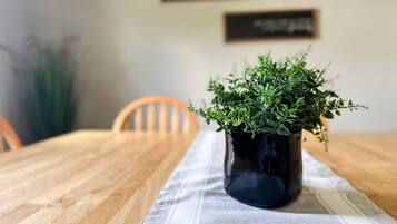 Uma mesa de madeira com um vaso escuro de plantas verdes sobre um pano de mesa branco.