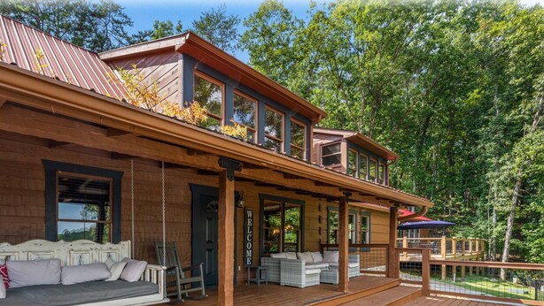 Une maison en bois à deux étages, dotée d’une terrasse, d’un porche couvert et d’une pancarte indiquant « Bienvenue ».