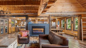 Un vaste espace de vie doté d’une cheminée, de poutres apparentes en bois et de grandes fenêtres.