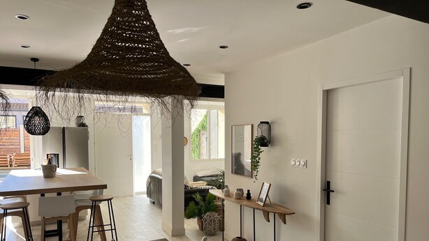Une cuisine moderne avec une table et des chaises en bois, un luminaire suspendu et une vue sur l’extérieur.