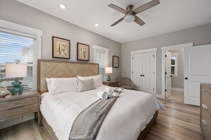 A bedroom with a bed, nightstands, a ceiling fan, and a view of the outside. - Baydream Believer | Soundfront, Pool & Hot Tub (Corolla)