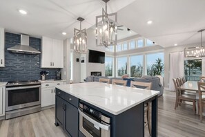 A modern kitchen with a large island, built-in appliances, and a dining area with a view. - Baydream Believer | Soundfront, Dock, Heated Pool & Hot Tub (Corolla)
