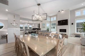 A modern kitchen with a dining area, large windows, and a flat-screen TV. - Baydream Believer | Soundfront, Dock, Heated Pool & Hot Tub (Corolla)