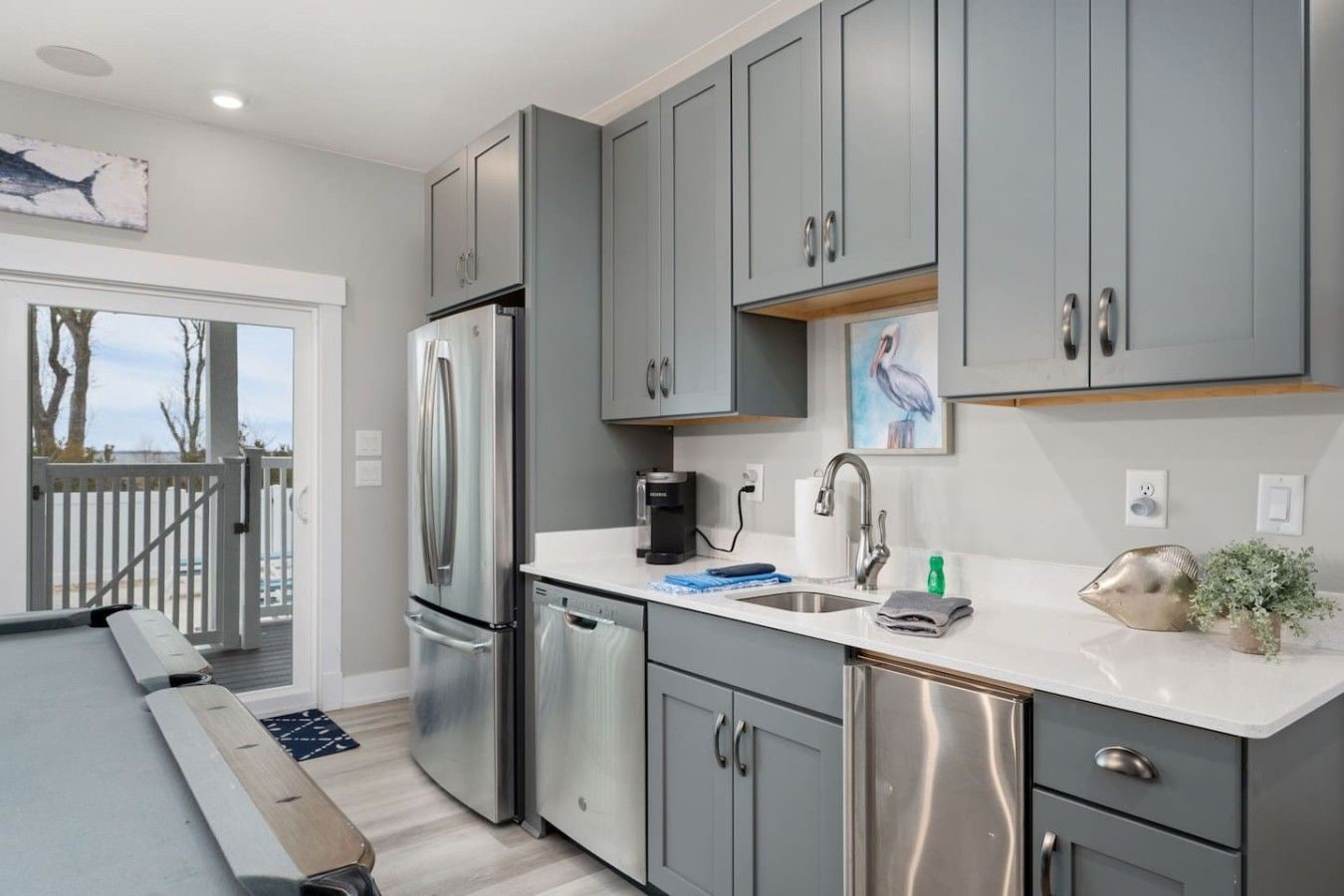 A modern kitchen with grey cabinets, stainless steel appliances, and a white countertop.