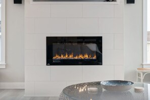 A modern fireplace with a glass front, a round glass table with a bowl and candles, and a white tiled wall.