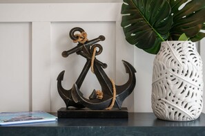 A decorative anchor sculpture on a dark surface, next to a white, intricately patterned vase with a large green plant. - Baydream Believer | Soundfront, Pool & Hot Tub (Corolla)