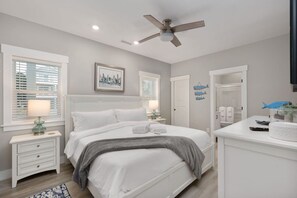 A bedroom with a bed, bedside tables, a ceiling fan, and a window with blinds. - Baydream Believer | Soundfront, Pool & Hot Tub (Corolla)