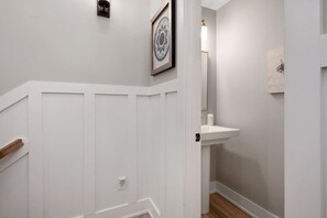 A hallway with a white door, a framed artwork on the wall, and a white sink with a mirror. - Baydream Believer | Soundfront, Pool & Hot Tub (Corolla)