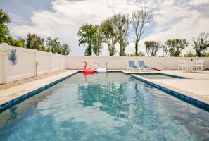 A rectangular swimming pool with clear blue water, surrounded by a white wall and a white fence.