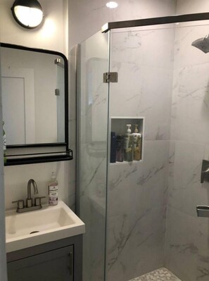 Bathroom features a glass-enclosed shower, shelf, and modern sink.