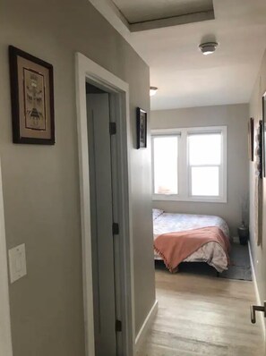 Enter a serene bedroom with a comfortable bed, framed artwork, and natural light pouring in through two windows.