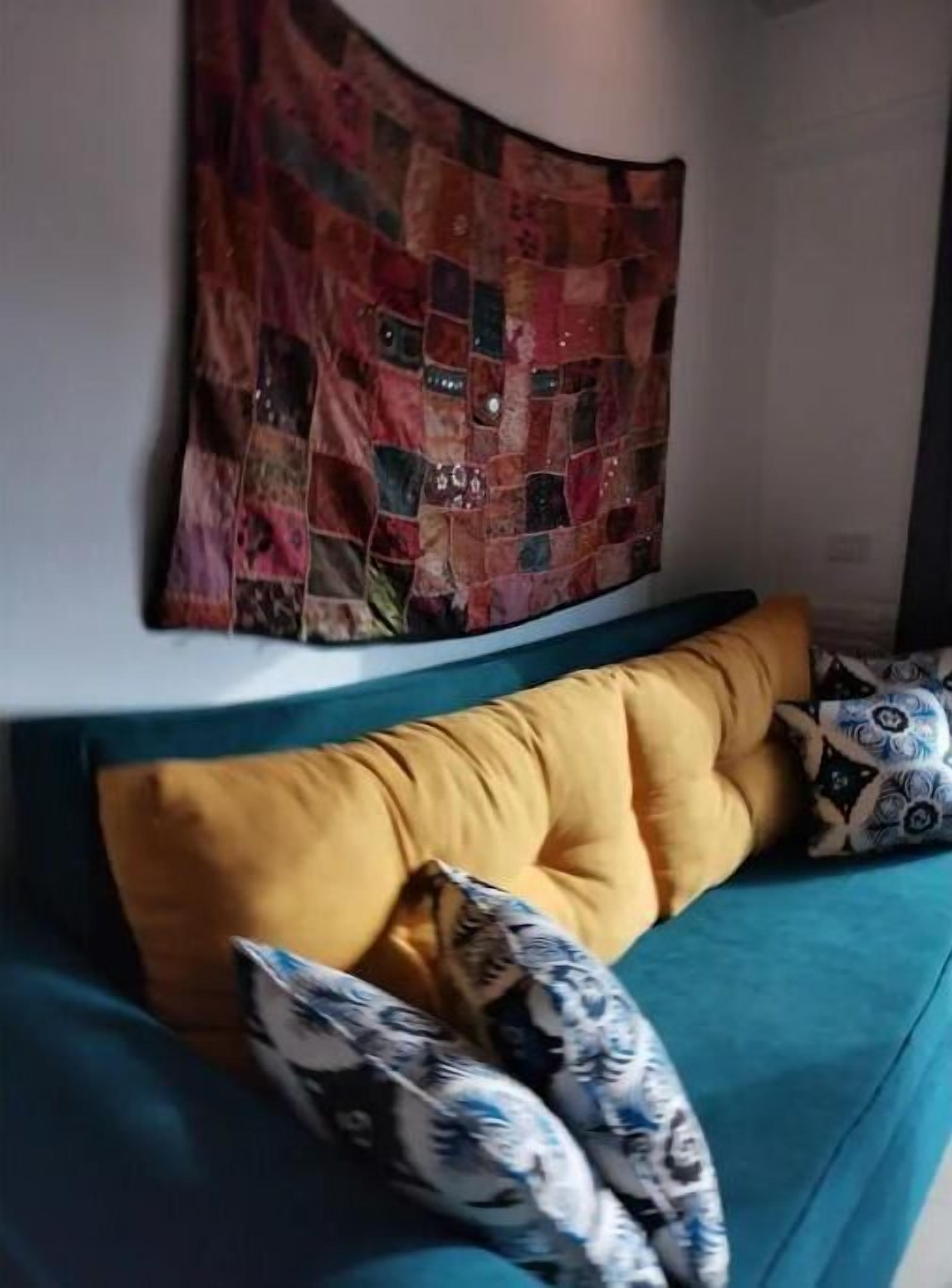 A teal sofa with mustard-colored cushions and patterned throw pillows.