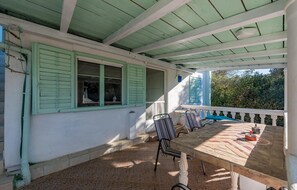 Relax in a charming outdoor space with a wooden table and two classic chairs, surrounded by lush greenery.