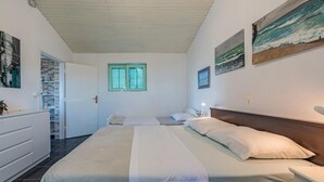 Une chambre avec un grand lit, une commode, une fenêtre avec des volets et des œuvres d’art accrochées aux murs.