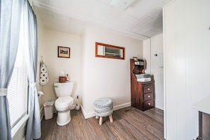 Ein Badezimmer mit Toilette, einem kleinen Hocker, einem Holzschrank und einem Spiegel an der Wand.