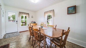 A dining room with a wooden table and chairs, a clock on the wall, and a window with curtains. - The Wrens Nest (Baltic)