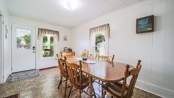 Une salle à manger avec une table et des chaises en bois, une horloge au mur et une fenêtre avec des rideaux.