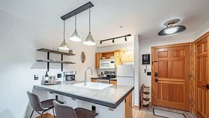 A compact kitchen with a central island, bar stools, pendant lighting, and wooden cabinets. - Basecamp Stays: Upscale Couple's Getaway, Hot Tubs (Driggs)