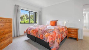 A bedroom with a bed, a wooden dresser, a nightstand, and a window with curtains. - All Inn - Spa Pool, Ride to Redwoods, Sleeps 8 (Rotorua)