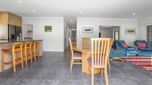 A modern kitchen with a dining area, bar stools, and blue armchairs. - All Inn - Spa Pool, Ride to Redwoods, Sleeps 8 (Rotorua)