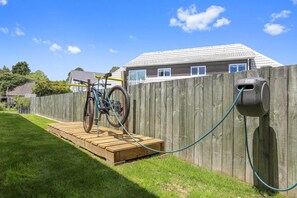 Een houten terras met een fiets en een tuinslang aangesloten op een apparaat aan de muur.