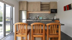 A modern kitchen with wooden cabinets, a stainless steel refrigerator, a microwave, and a large island with bar stools. - All Good - MTB Base, Bike Wash, Sleeps 4 (Rotorua)