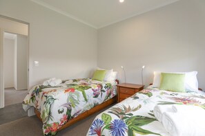 A bedroom with two single beds, each with floral bedding, a nightstand, and a bedside table. - All Good - MTB Base, Bike Wash, Sleeps 4 (Rotorua)