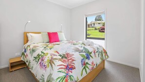 A bedroom with a bed, a nightstand, a window with a view of a house and garden. - All Good - MTB Base, Bike Wash, Sleeps 4 (Rotorua)