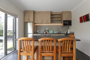 A modern kitchen with wooden cabinets, a stainless steel refrigerator, a microwave, and a large window. - All Good - MTB Base, Bike Wash, Sleeps 4 (Rotorua)