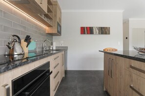A modern kitchen with wooden cabinets, a black countertop, and a stainless steel kettle. - All Good - MTB Base, Bike Wash, Sleeps 4 (Rotorua)
