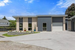 Een modern gebouw met twee verdiepingen, een garage, een aangelegde voortuin en een heldere lucht.