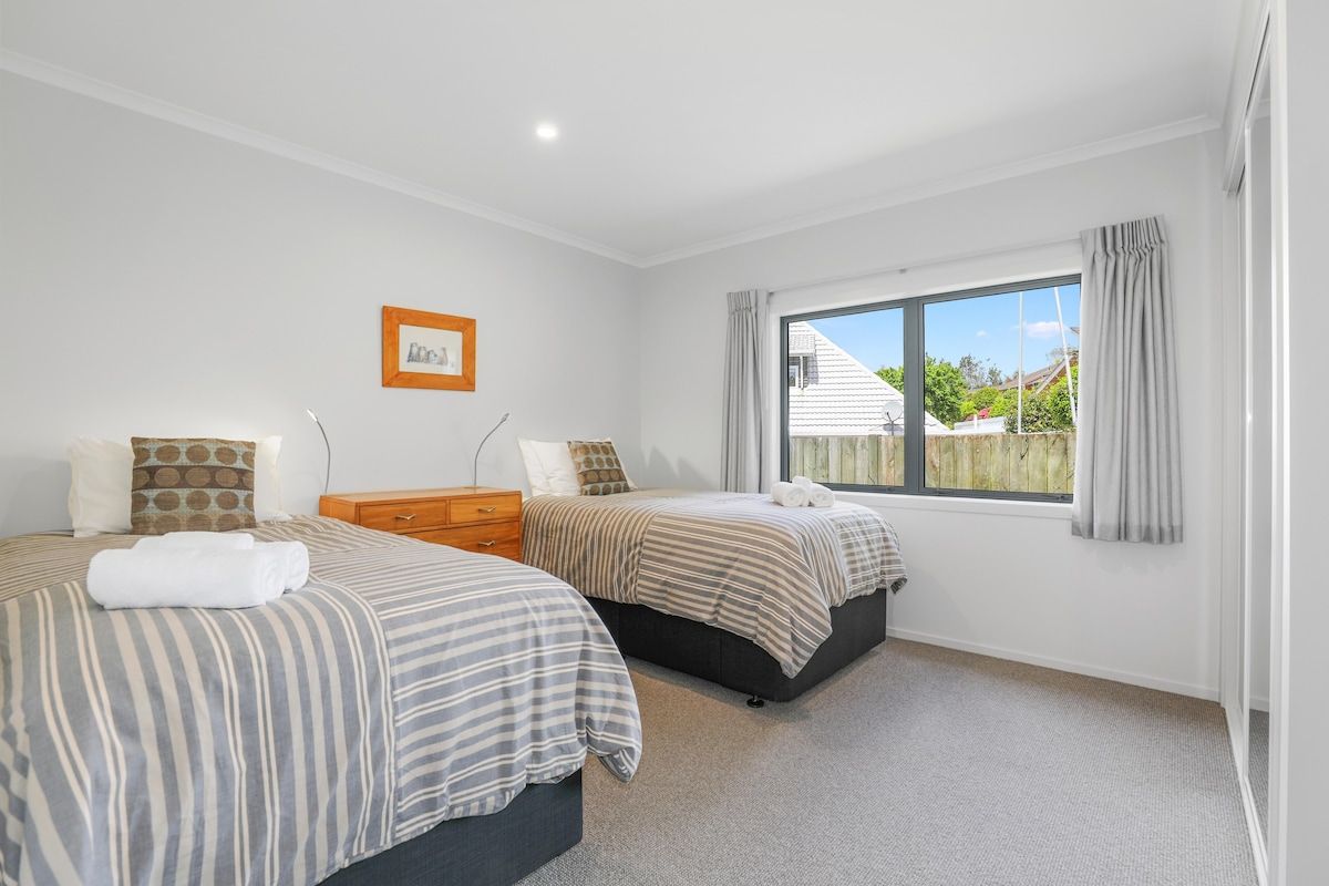 A bedroom with two beds, a window with curtains, and a framed picture on the wall.