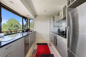 A modern kitchen with stainless steel appliances, a glass backsplash, and a view of greenery outside. - Pukeko Landing - Lake Views, Spa Pool, Sleeps 7 (Rotorua)
