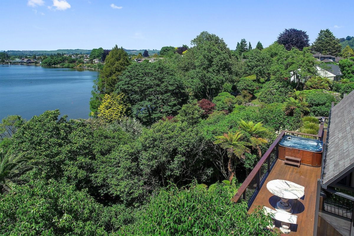 Een hottub op een houten terras met uitzicht op een meer en omliggende bomen.