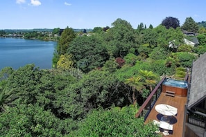 A rooftop with a hot tub, surrounded by dense greenery and overlooking a lake. - Pukeko Landing - Lake Views, Spa Pool, Sleeps 7 (Rotorua)
