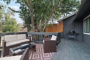 A deck with outdoor furniture, a grill, and a tree providing shade.