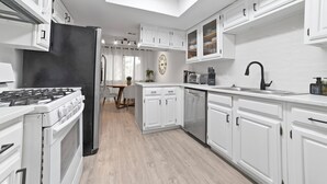 A modern kitchen with white cabinetry, a black refrigerator, a stove, and a dishwasher. - Modern Home 7 Min from Downtown (Austin)