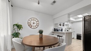 A modern kitchen with white cabinets, a wooden dining table, and a large wall clock. - Modern Home 7 Min from Downtown (Austin)