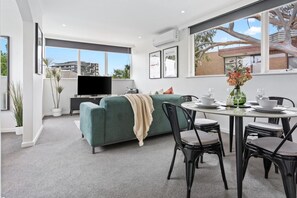 Un salon moderne avec un canapé vert, une table à manger avec des chaises et un téléviseur à écran plat.