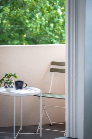 Un petit balcon avec une table blanche, une tasse noire et une plante en pot.