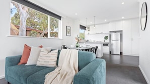 A modern kitchen with white cabinets, a stainless steel refrigerator, and a dining area with a table and chairs. - Charnwood 2BR: Homely Haven (St Kilda)
