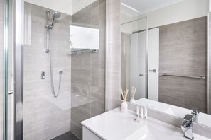 Une salle de bain moderne avec une douche à parois de verre, un lavabo blanc avec un miroir et un porte-serviettes.