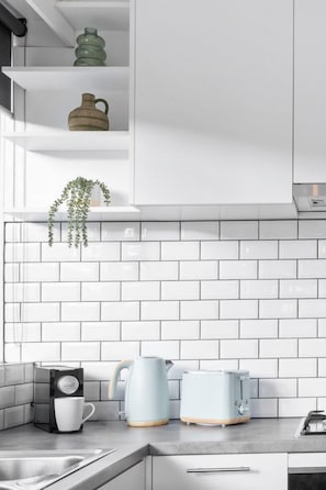 A kitchen with white cabinets, a tiled backsplash, a hanging plant, a coffee maker, and a toaster.