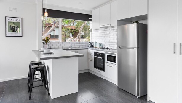A modern kitchen with white cabinetry, a stainless steel refrigerator, a built-in oven, and a large window offering a view of the outdoors. - Charnwood 2BR: Homely Haven (St Kilda)